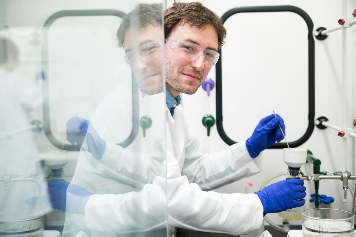 A man in a lab coat and glasses conducts research in a laboratory setting, focused on his work.