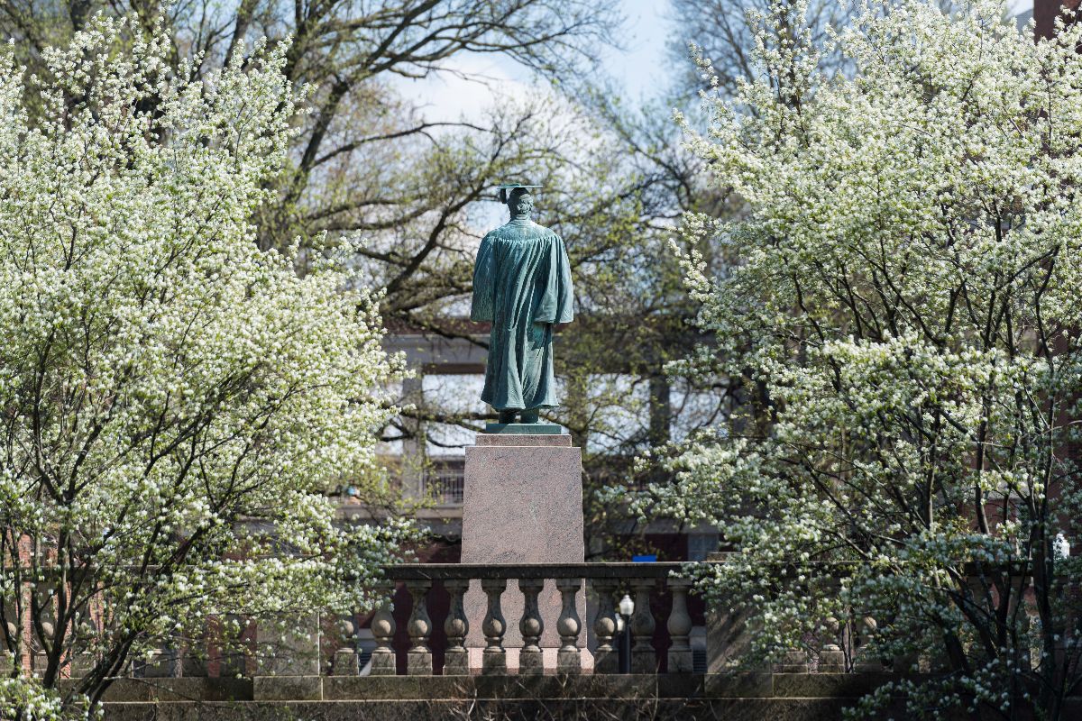 A statue of a man seated on a bench in front of a university building at the University of Rochester campus.